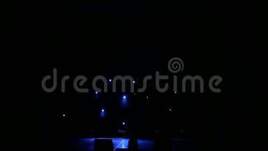 蓝光在黑暗中在一个空的舞台上闪烁着白色的光芒。 舞台照明
